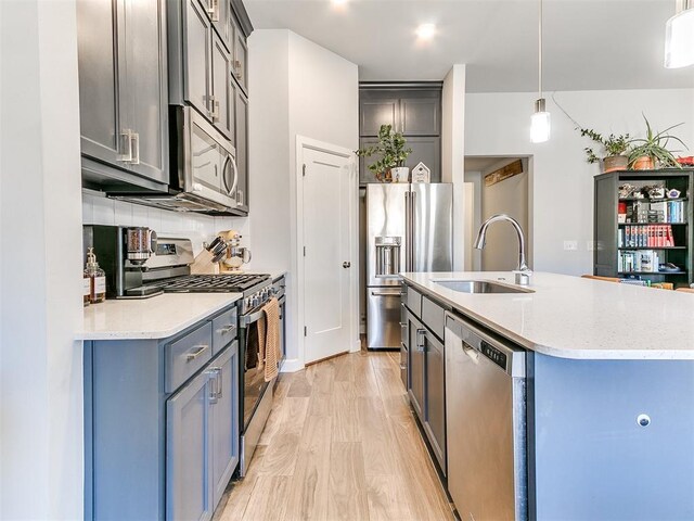 kitchen featuring appliances with stainless steel finishes, sink, decorative light fixtures, a center island with sink, and light hardwood / wood-style floors