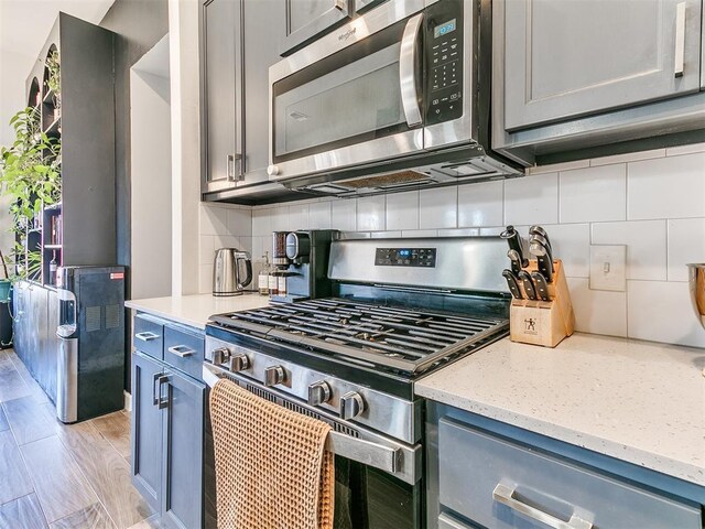 kitchen with backsplash, stainless steel appliances, light hardwood / wood-style flooring, and light stone counters