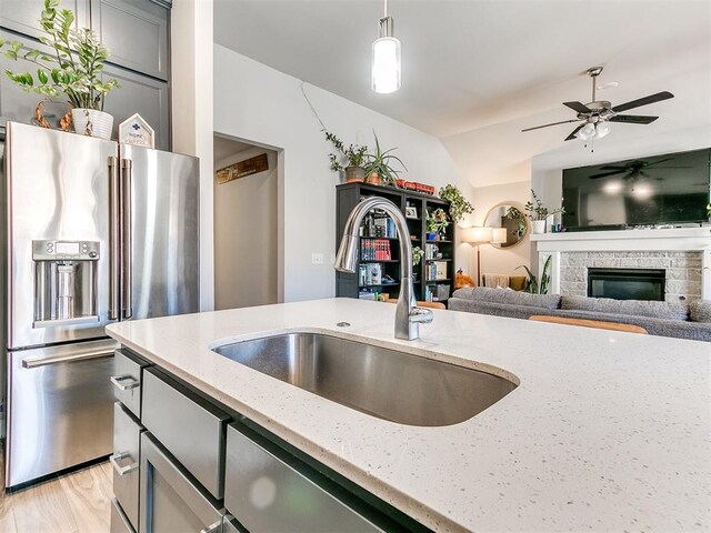 kitchen with light stone countertops, high end refrigerator, sink, decorative light fixtures, and a stone fireplace