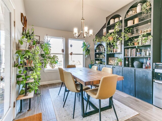 dining area with hardwood / wood-style floors, vaulted ceiling, and a notable chandelier