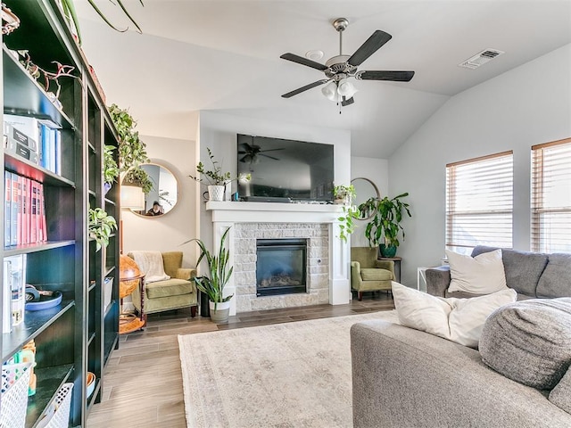 living room with light wood-type flooring, ceiling fan, lofted ceiling, and a stone fireplace