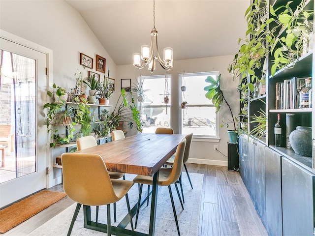 dining room with light wood-type flooring, vaulted ceiling, and a notable chandelier