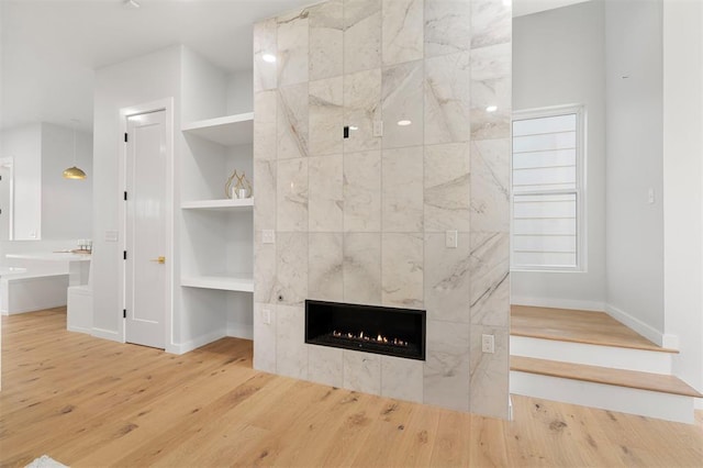 unfurnished living room with built in features, wood-type flooring, and a tile fireplace