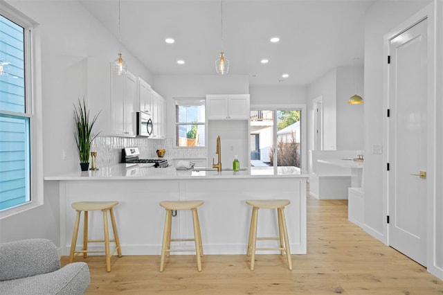 kitchen featuring white cabinets, appliances with stainless steel finishes, a kitchen bar, hanging light fixtures, and kitchen peninsula