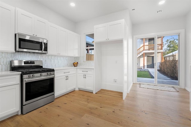 kitchen featuring decorative backsplash, white cabinetry, stainless steel appliances, and light wood-type flooring