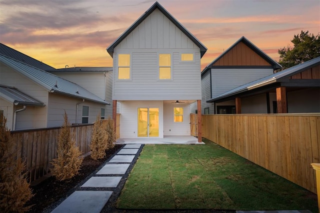 back house at dusk with a patio area and a lawn