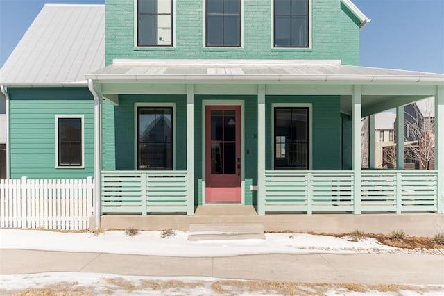 view of front facade with covered porch, fence, metal roof, and brick siding