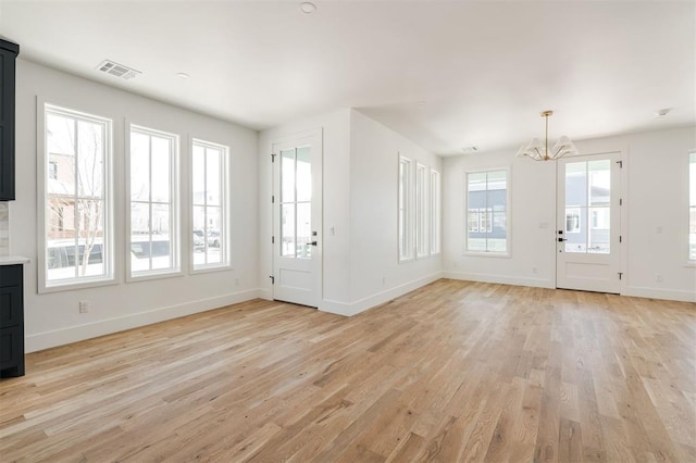 unfurnished living room with baseboards, a notable chandelier, visible vents, and light wood-style floors