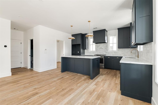 kitchen featuring stainless steel range, decorative backsplash, light wood-type flooring, premium range hood, and a sink