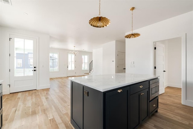 kitchen featuring light wood-style floors, pendant lighting, stainless steel microwave, and visible vents