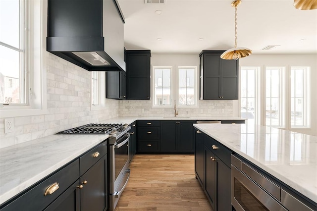 kitchen featuring backsplash, appliances with stainless steel finishes, a sink, wall chimney range hood, and light wood-type flooring