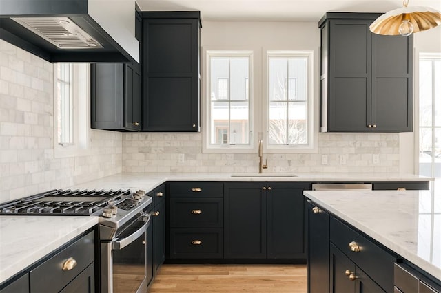 kitchen with light wood-style floors, light stone counters, stainless steel appliances, wall chimney range hood, and a sink