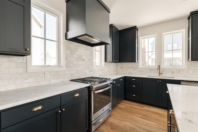 kitchen featuring a wealth of natural light, stainless steel range with gas stovetop, a sink, and wall chimney range hood