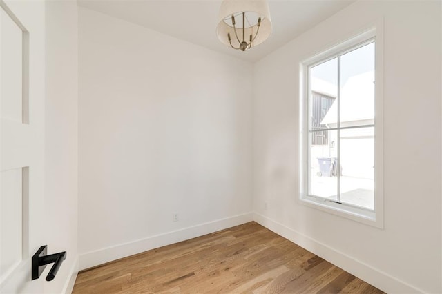 unfurnished room with light wood-style floors, a wealth of natural light, a notable chandelier, and baseboards