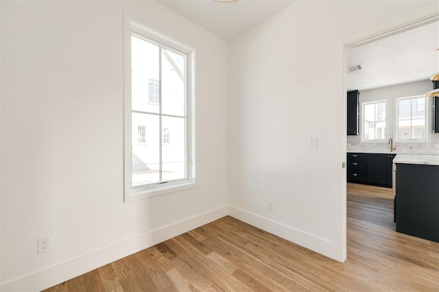 empty room featuring visible vents, a sink, light wood-style flooring, and baseboards