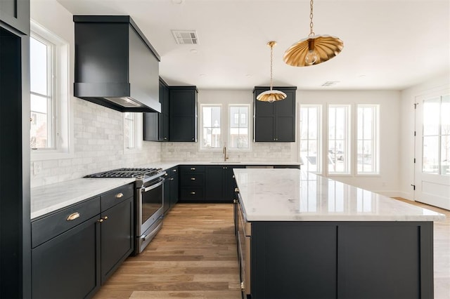 kitchen featuring visible vents, light wood-style floors, a kitchen island, wall chimney range hood, and gas stove