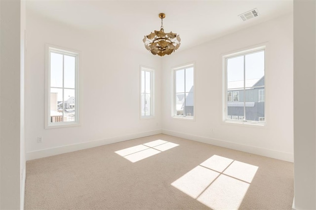 carpeted empty room with visible vents, baseboards, and an inviting chandelier