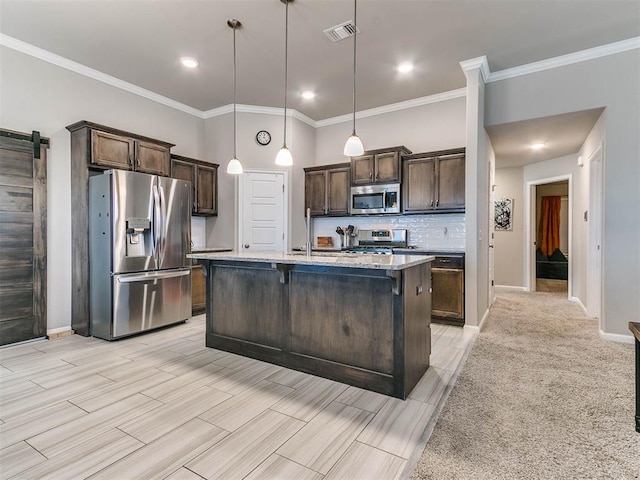 kitchen featuring light stone countertops, appliances with stainless steel finishes, a barn door, decorative light fixtures, and a center island with sink