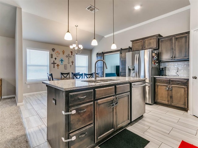 kitchen with a kitchen island with sink, hanging light fixtures, sink, a barn door, and appliances with stainless steel finishes