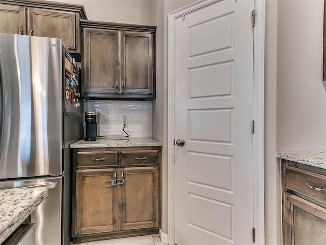 kitchen featuring decorative backsplash, stainless steel fridge, light stone counters, and dark brown cabinetry