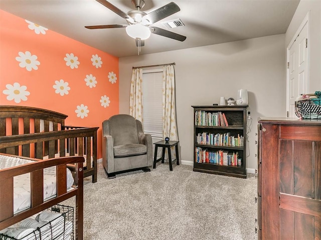 carpeted bedroom featuring a nursery area and ceiling fan