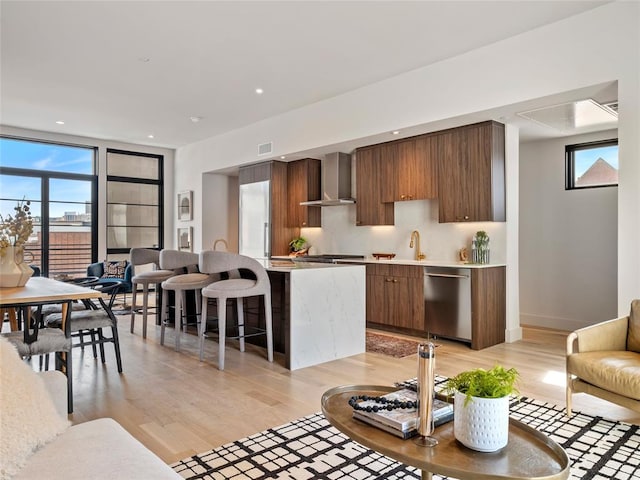 kitchen featuring wall chimney exhaust hood, light hardwood / wood-style floors, dishwasher, and plenty of natural light