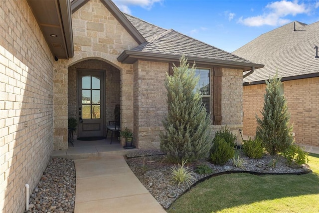 entrance to property featuring brick siding, stone siding, and roof with shingles