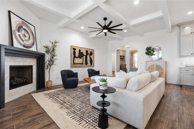 living area featuring baseboards, beam ceiling, a fireplace, arched walkways, and dark wood-type flooring