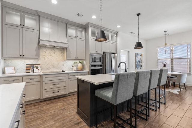 kitchen featuring visible vents, a breakfast bar area, light countertops, appliances with stainless steel finishes, and custom exhaust hood