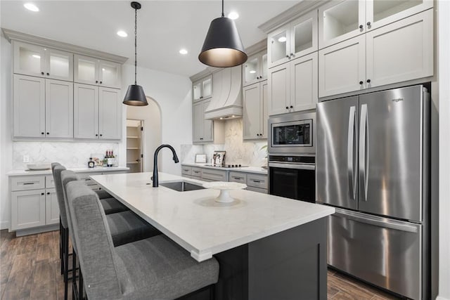 kitchen featuring dark wood-style floors, a center island with sink, a sink, stainless steel appliances, and a kitchen bar