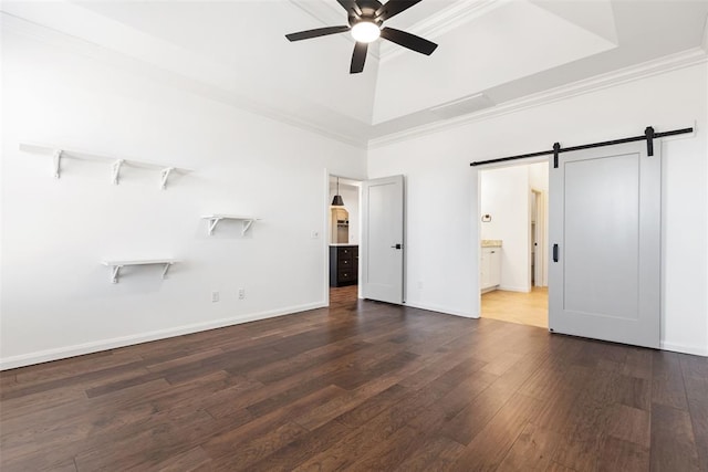 unfurnished bedroom featuring crown molding, baseboards, a barn door, wood finished floors, and a raised ceiling