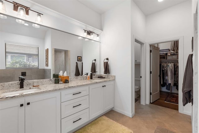 full bath with toilet, a sink, tiled shower, double vanity, and baseboards