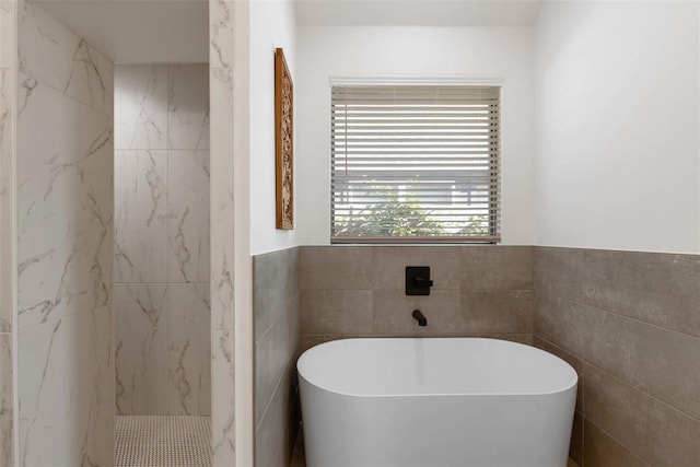 full bath featuring tile walls, a freestanding tub, a wainscoted wall, and a marble finish shower