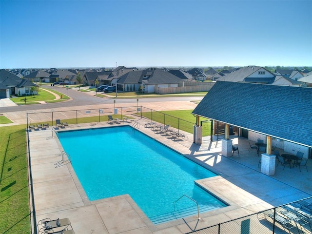 pool with a patio area, a residential view, a lawn, and fence