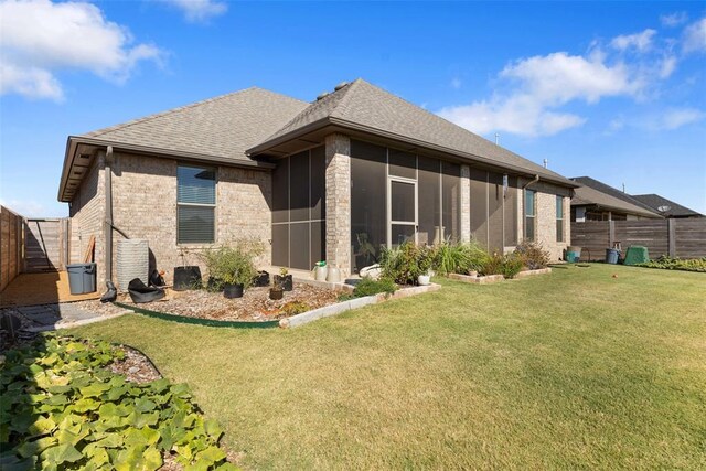 14704 Ashore Dr, Oklahoma City, OK 73142 - back of house featuring brick siding, a fenced backyard, a shingled roof, a sunroom, and a lawn