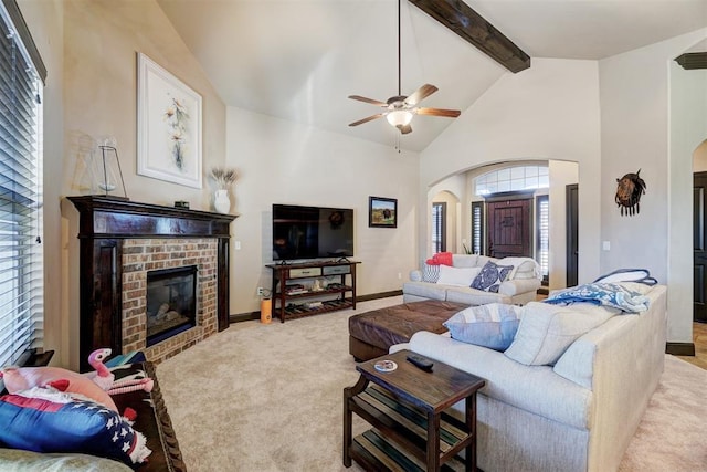 carpeted living room featuring a brick fireplace, high vaulted ceiling, beam ceiling, and ceiling fan