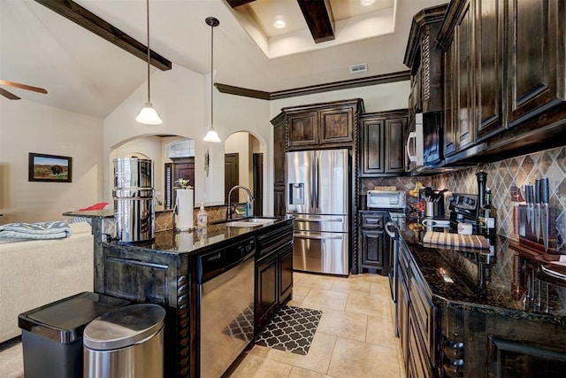 kitchen with decorative light fixtures, stainless steel appliances, dark stone counters, an island with sink, and sink