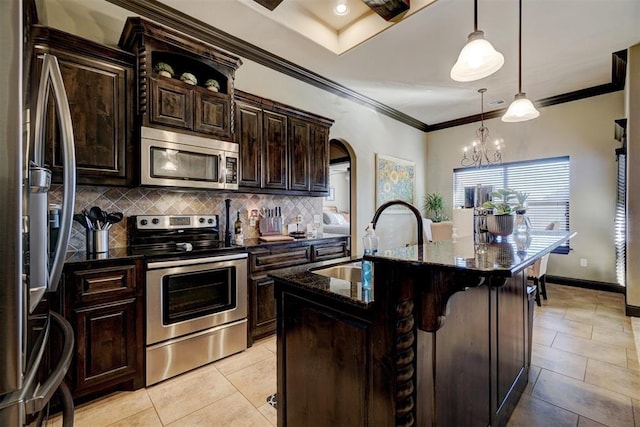 kitchen featuring stainless steel appliances, decorative backsplash, a kitchen island with sink, dark stone counters, and pendant lighting