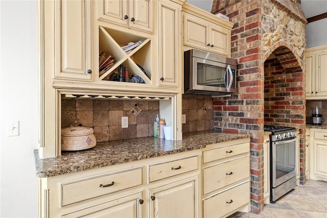 kitchen featuring appliances with stainless steel finishes, cream cabinets, decorative backsplash, and dark stone countertops