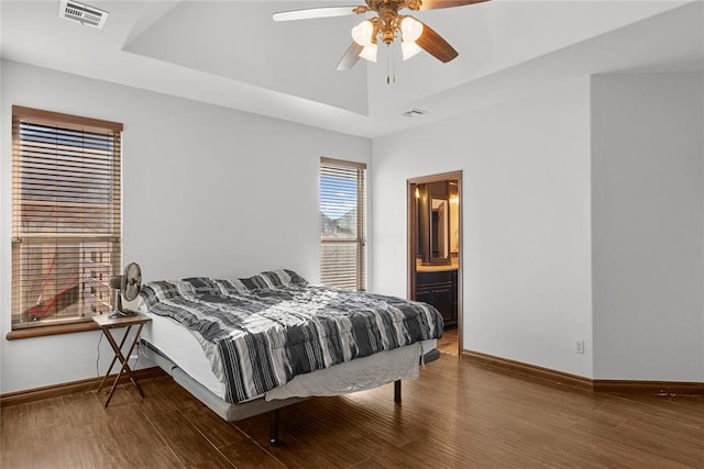 bedroom with a raised ceiling, dark hardwood / wood-style flooring, connected bathroom, and ceiling fan