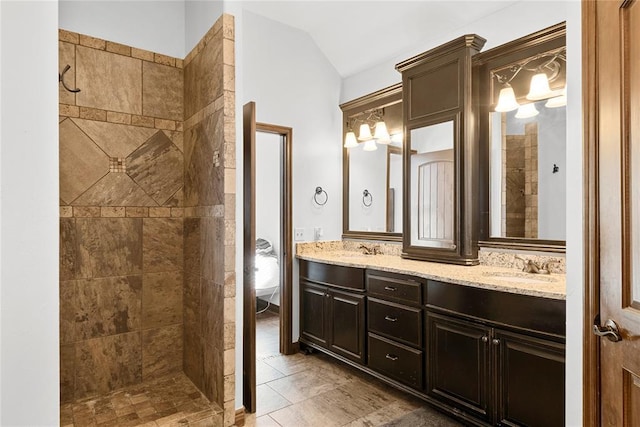 bathroom with vaulted ceiling, tiled shower, and vanity