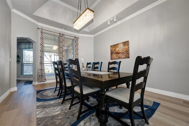 dining area featuring a raised ceiling, ornamental molding, wood-type flooring, and an inviting chandelier