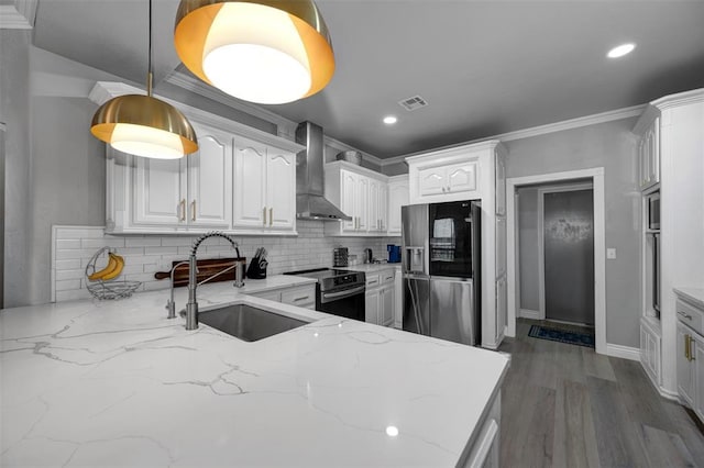 kitchen with stainless steel appliances, sink, wall chimney range hood, pendant lighting, and white cabinets