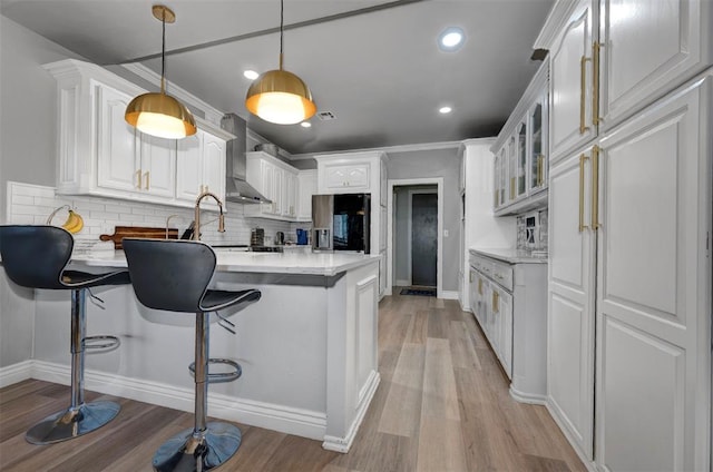 kitchen featuring white cabinets, light wood-type flooring, wall chimney range hood, and hanging light fixtures