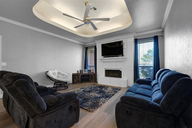 living room featuring ceiling fan, a raised ceiling, wood-type flooring, and a brick fireplace