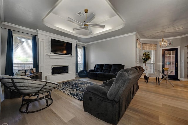 living room featuring a tray ceiling, ceiling fan, light hardwood / wood-style floors, and a brick fireplace