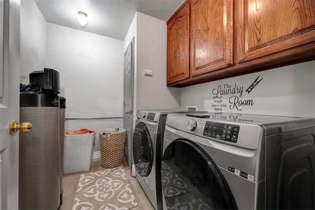 laundry room with washing machine and dryer, water heater, cabinets, and light wood-type flooring