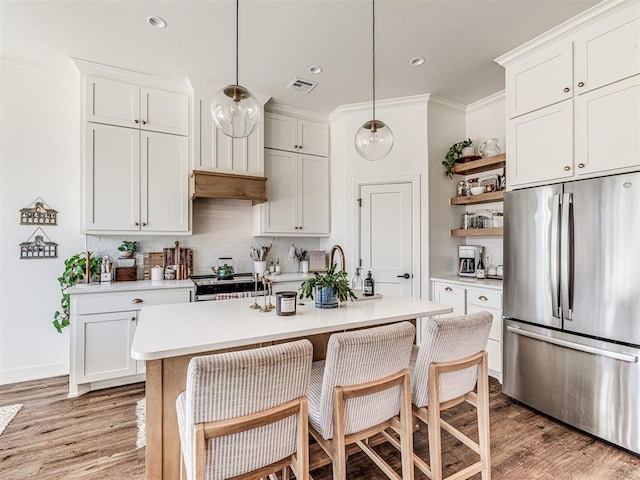 kitchen with white cabinetry, hanging light fixtures, stainless steel appliances, an island with sink, and decorative backsplash