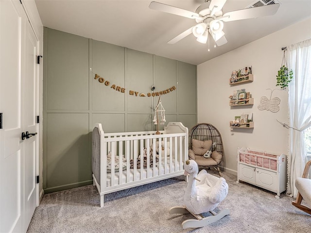 bedroom featuring a nursery area, light colored carpet, and ceiling fan