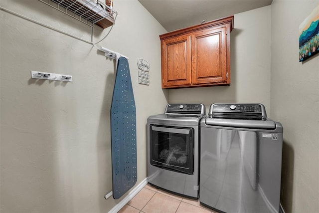 clothes washing area featuring cabinets, washing machine and dryer, and light tile patterned floors